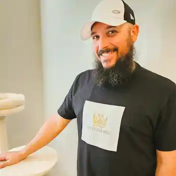 A man with a beard wearing a hat standing in front of a sink.