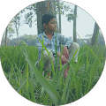 A boy sitting in the grass near some trees