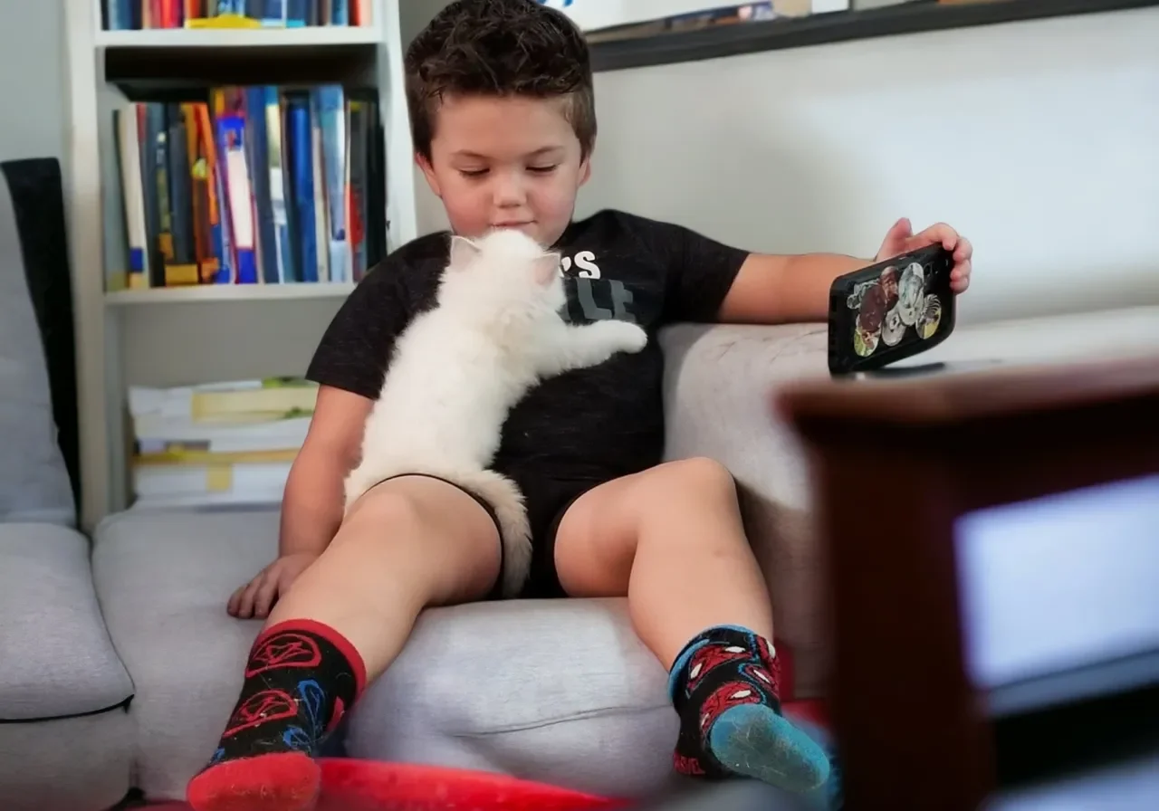 A boy sitting on the couch with his cat.